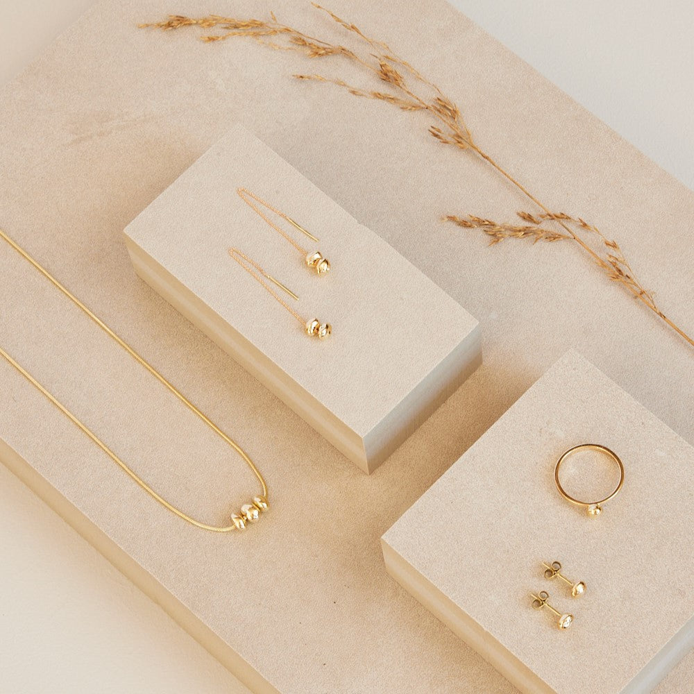 Collectie Essentials, minimalistische gouden sieraden met 14 karaat gouden steentjes aan een ketting, oorhangers, oorstekers en ring.