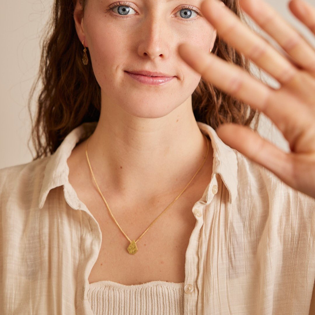 Model draagt ketting met 18 karaat gouden hanger "Imperfectie Rocks". Van gezicht tot borst in beeld met hand vooruit gestoken.