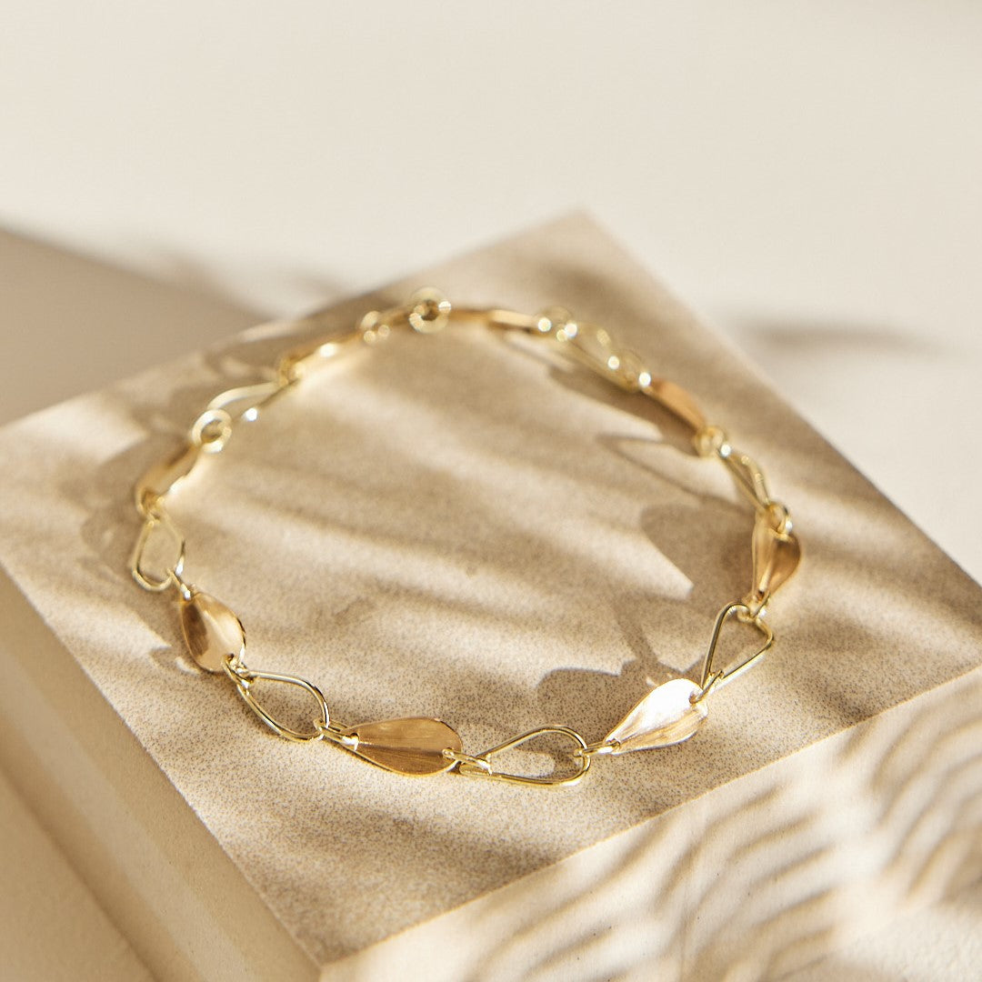 Gouden armband Leaves met afwisselend open en dichte blaadjes. Liggend op een steen in schaduw van een varenblad.